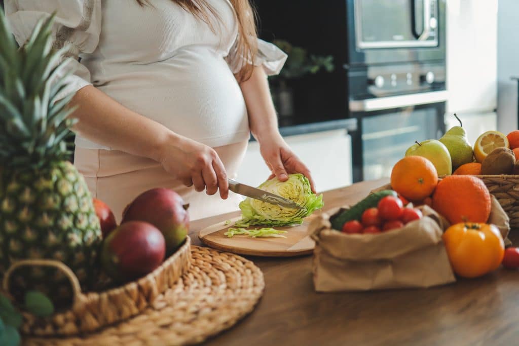 Pregnant woman making salad in her kitchen healthcare