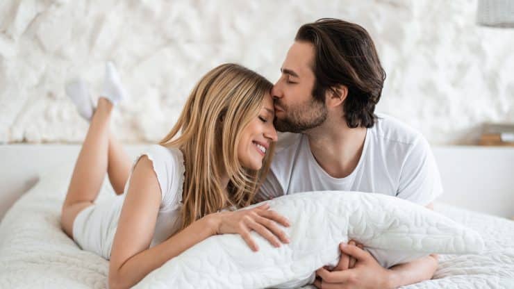 Affectionate young Caucasian couple hugging and kissing in bed expressing affection at home